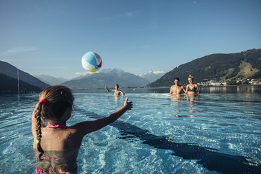 Family enjoying water fun at the outdoor pool with mountain scenery in the background, child playing with a ball in the water. | © Korbinian Seifert