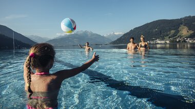 Family enjoying water fun at the outdoor pool with mountain scenery in the background, child playing with a ball in the water. | © Korbinian Seifert