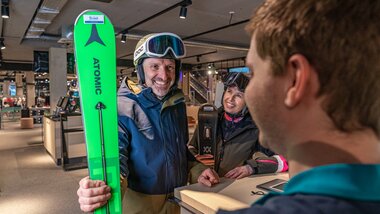 A person receives ski equipment at the Schmitten ski rental counter and is smiling happily. | © Max Bründl