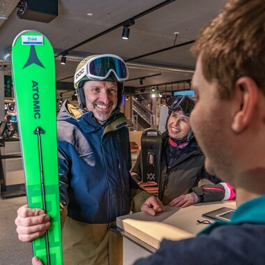 A person receives ski equipment at the Schmitten ski rental counter and is smiling happily. | © Max Bründl