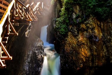 The Sigmund Thun Gorge features a dramatic mountain canyon with a waterfall and wooden walkway in a nature reserve. | © Neumayr/RH