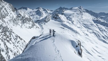 Mountaineers on snowy summit in the Austrian Alps with a wide view of snow-covered mountains. | © Kitzsteinhorn