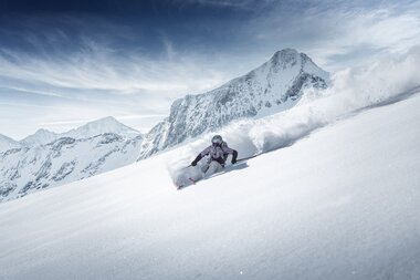 Skier carving through deep snow in mountain terrain with cloudy sky. | © Kitzsteinhorn