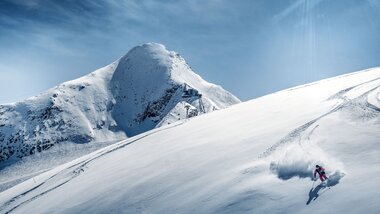 Skier descending on a snowy, steep mountain slope with a mountain in the background | © Kitzsteinhorn