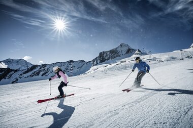 Skieriders on a glacier ski slope under a cloudy sky with the sun shining | © Kitzsteinhorn