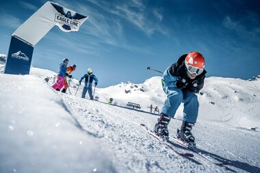 Skier racer on the slope at Kitzsteinhorn with a banner and snow-covered mountain in the background. | © Kitzsteinhorn