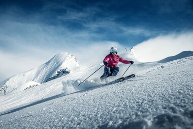 Skier carving through snow on slopes at Kitzsteinhorn with mountain and sky in the background. | © Kitzsteinhorn