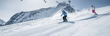 Skier on a snowy slope with mountain in the background, in a ski resort with cable cars in the mountains. | © Kitzsteinhorn