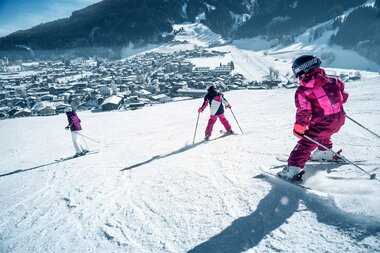 Family skiing on a snowy slope overlooking a mountain village in winter | © Kitzsteinhorn