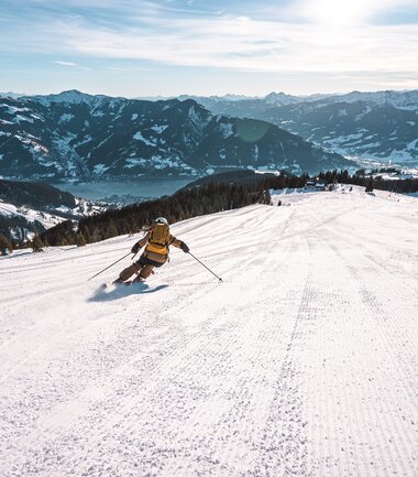 Skier carving down a snowy slope in the mountains of Austria at sunrise | © Schmittenhöhebahn AG