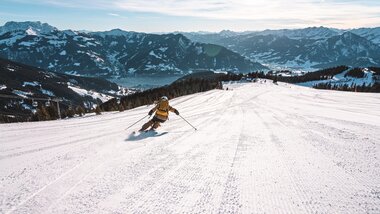 Skier carving down a snowy slope in the mountains of Austria at sunrise | © Schmittenhöhebahn AG