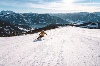Skier carving down a snowy slope in the mountains of Austria at sunrise | © Schmittenhöhebahn AG