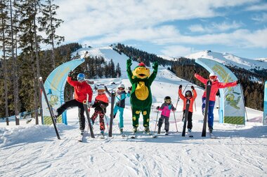 Group of skiers with a mascot character on a snowy mountain, sunny weather. | © Zell am See-Kaprun Tourismus
