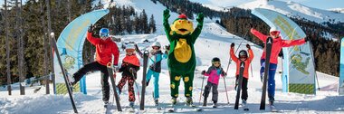 Group of skiers with a mascot character on a snowy mountain, sunny weather. | © Zell am See-Kaprun Tourismus
