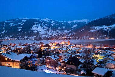 Lights shine in a snow-covered mountain town at night, surrounded by snowy mountains. | © Christian Mairitsch
