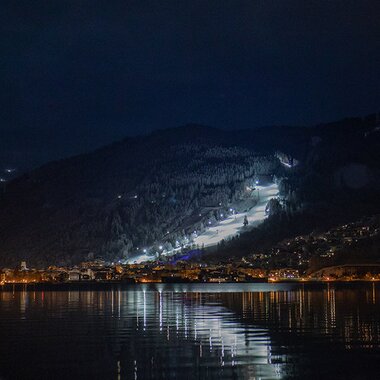 Night skiing on Schmittenhöhe with illuminated slopes reflected in the water. | © Schmittenhöhe