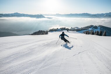 Skier skier on fresh snow slope under a sunny sky with mountains in the background. | © Johannes Radlwimmer