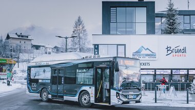 A modern electric minibus parked in front of a modern building in snowy Kaprun, Austria. | © Kitzsteinhorn