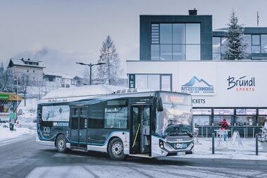 A modern electric minibus parked in front of a modern building in snowy Kaprun, Austria. | © Kitzsteinhorn