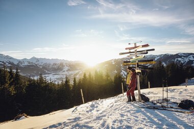 Ski tourer in the snow with a signpost, mountain scenery, and sunset in Zell am See-Kaprun. | © Seifert