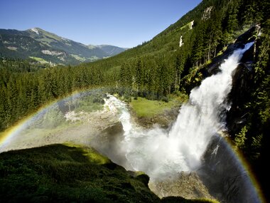 Krimmler Waterfalls surrounded by a scenic mountain landscape with a rainbow in front. | © Michael Huber