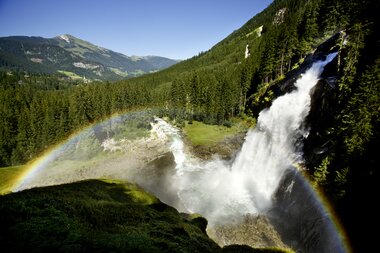 Krimmler Waterfalls surrounded by a scenic mountain landscape with a rainbow in front. | © Michael Huber