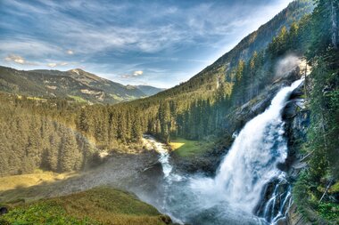The Krimmler Waterfall in a scenic mountain landscape with green forest and blue sky. | © Christian Mairitsch
