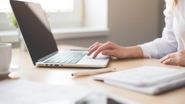 A person working on a laptop at a bright desk in daylight.