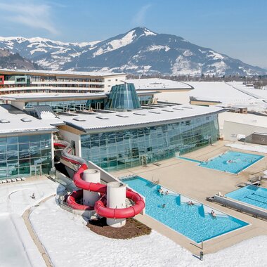 Aerial view of Tauern Spa in winter snow, featuring water slides, pools, and modern architecture surrounded by mountains. | © Tauern SPA Zell am See-Kaprun