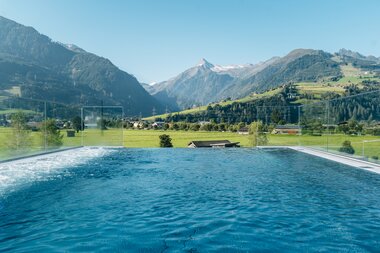 Pool overlooking green fields and mountains in the Tauern SPA area with snow-capped peaks in the background. | © Zell am See-Kaprun Tourismus
