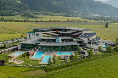 Modern spa resort with outdoor pools surrounded by green fields and mountains in the background. | © TAUERN SPA Zell am See-Kaprun