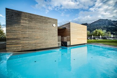 Exterior view of the Mountain Crystal Sauna at Tauern Spa in Kaprun, with a swimming pool, blue sky, and mountains in the background. | © TAUERN SPA Zell am See-Kaprun