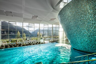 Indoor wellness and water park with a large pool, modern architecture, and large windows showing a scenic mountain landscape. | © TAUERN SPA Zell am See-Kaprun