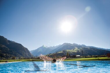 Person swimming in an outdoor pool amidst scenic mountain landscape at sunrise. | © Günther Böck