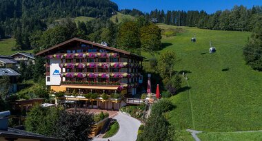 Sporthotel Alpin in a mountain landscape with green meadows and ski lifts in the background. | © Sporthotel Alpin Zell am See