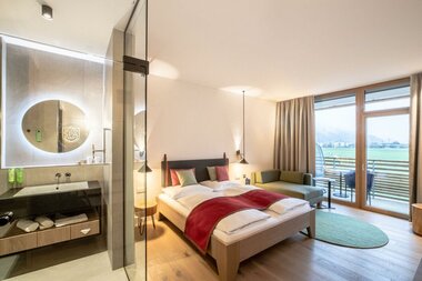 Modern double room with terrace view and access to a bathroom with mirror and sink. | © TAUERN SPA Zell am See-Kaprun