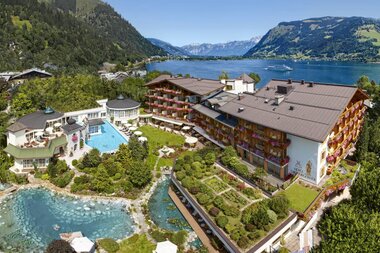 View of a hotel with two pools in a mountainous landscape with a lake in the background. | © Hotel Salzburgerhof