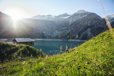 Hikers near Hochgebirgsstauseen with lake and mountain views on a sunny day. | © Zell am See-Kaprun Tourismus