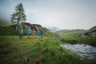 Group hiking on a green hillside with a stream and forests in the background. | © Kitzsteinhorn