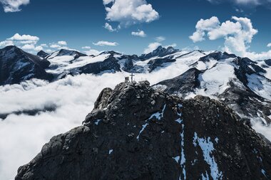 Mountain summit on Kitzsteinhorn with snow patches and surrounding peaks under a blue sky with clouds. | © Kitzsteinhorn