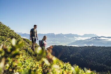 Two hikers on a narrow mountain meadow overlooking mountains and the sky. | © Korbinian Seifert
