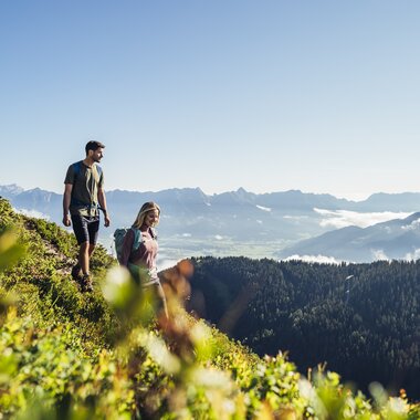 Two hikers on a narrow mountain meadow overlooking mountains and the sky. | © Korbinian Seifert