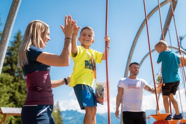 Family playing on a swing at an amusement park on a sunny day. | © Branislav Rohal