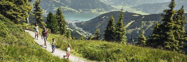 Family hiking on a gravel trail in green mountain scenery with lakes and mountains in the background. | © Korbinian Seifert