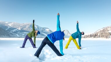People practicing yoga in the snow with a snowy mountain landscape, in various poses, in cool weather. | © Artisual