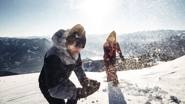 People playing in the snow on the Schmittenhöhe in Zell am See-Kaprun, surrounded by mountains under sunshine. | © Zell am See-Kaprun Tourismus